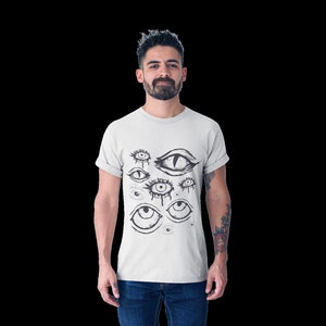 May include: A white t-shirt with a black and white graphic print of multiple eyes. The eyes are drawn in a stylized, abstract style.