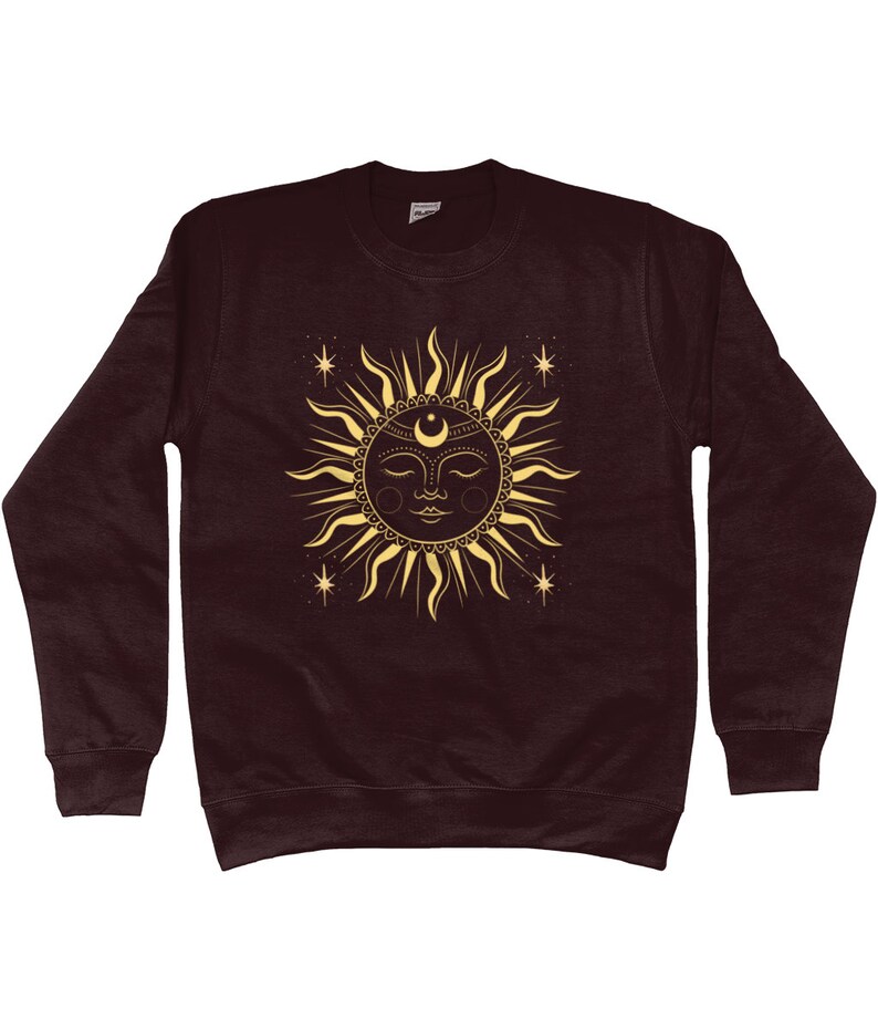 May include: A maroon sweatshirt with a gold sun and moon design. The sun has a face with closed eyes and a crescent moon above it. There are small stars around the sun.