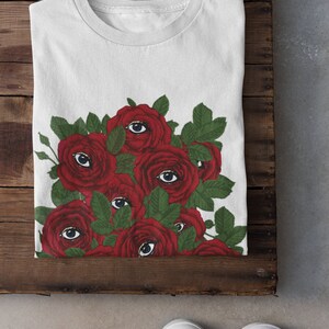 May include: White t-shirt with a graphic of red roses with eyes on them.