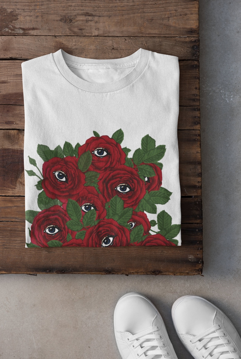 May include: White t-shirt with a graphic of red roses with eyes on them.