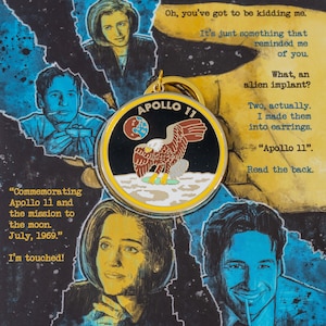 May include: A gold-colored pin with a black and white image of an eagle landing on the moon. The pin says "APOLLO 11" in a yellow banner. The text "Commemorating Apollo 11 and the mission to the moon. July, 1969." is written below the pin.