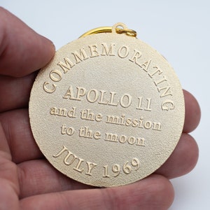 May include: Gold-colored metal keychain commemorating Apollo 11 and the mission to the moon in July 1969.