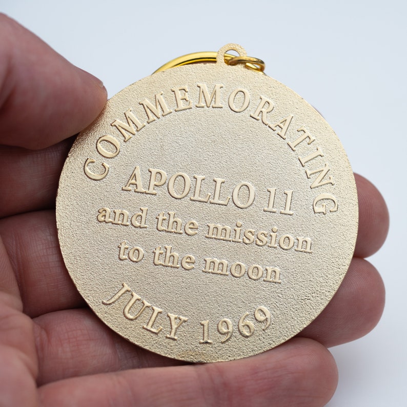 May include: Gold-colored metal keychain commemorating Apollo 11 and the mission to the moon in July 1969.