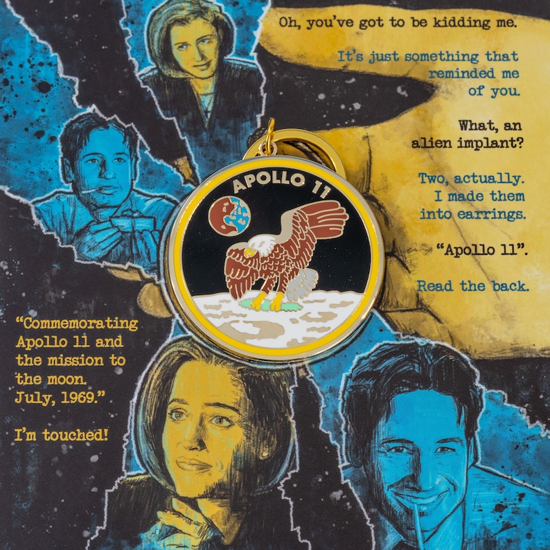 May include: A gold-colored pin with a black and white image of an eagle landing on the moon. The pin says "APOLLO 11" in a yellow banner. The text "Commemorating Apollo 11 and the mission to the moon. July, 1969." is written below the pin.