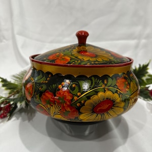 May include: A hand-painted wooden bowl with a lid. The bowl is black with gold trim and is decorated with orange, yellow, and green floral designs. The lid has a small red knob.