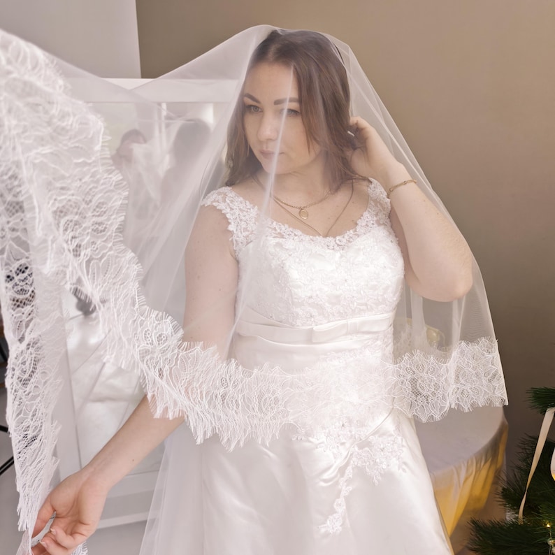 Bride wearing lace veil with blusher covering face, light ivory cathedral style