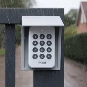May include: A white keypad with black buttons and the brand name "frient" is mounted on a grey metal post. The keypad has numbers 0-9 and a hash symbol. The keypad is protected by a small, grey, angled cover. Rain is falling.