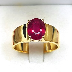 Op de afbeelding: Een gouden ring met een grote, ovale robijn. De robijn is diep rood van kleur en is gezet in een eenvoudige, gepolijste gouden band.