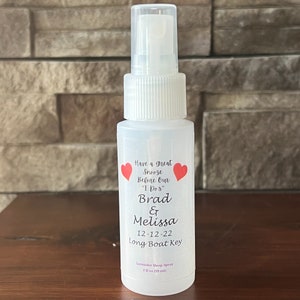 Op de afbeelding: Een transparante plastic spuitfles met een wit etiket. Het etiket heeft rode harten en zwarte tekst die "Have a great snooze before our "I Do's" Brad & Melissa 12-12-22 Long Boat Key" en "Lavender Sleep Spray 2 fl oz (59 ml)" luidt.