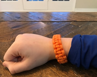 May include: A bright orange paracord bracelet with a woven design.