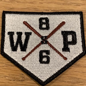 May include: White and black embroidered patch shaped like a baseball diamond with the letters "W" and "P" on either side of a brown wooden baseball bat with the number "8" above the bat and the number "6" below the bat.