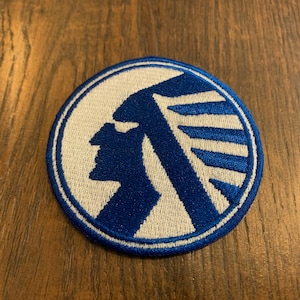 May include: A blue and white embroidered patch with a Native American profile in a circle.