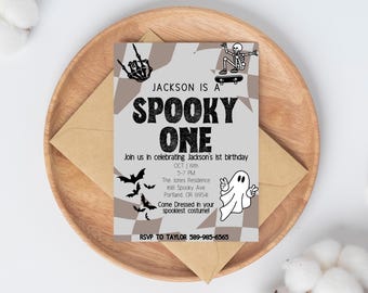 May include: A Halloween-themed invitation with the text "Jackson is a Spooky One." The invitation features a skeleton on a skateboard, bats, and a ghost. The invitation is on a wooden plate with a brown envelope.