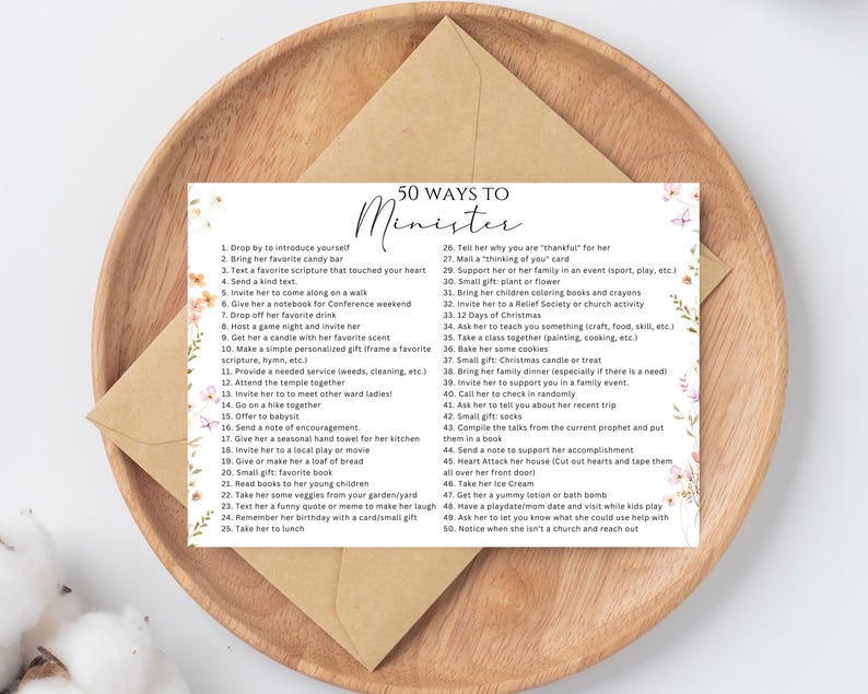 May include: A printed card with the text "50 Ways to Minister" on a wooden tray. The card lists 50 suggestions for acts of service, with floral and butterfly accents. An envelope rests behind the card.