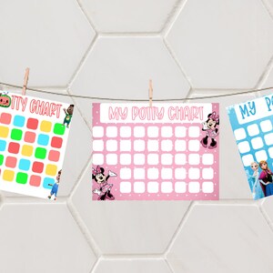 May include: Three colorful potty charts hang from a string with clothespins. The charts feature characters from Cocomelon, Minnie Mouse, and Frozen. Each chart has a grid of squares for tracking progress, with the words "MY POTTY CHART" at the top.