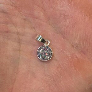 May include: A silver pendant with a round, clear glass charm filled with iridescent glitter.