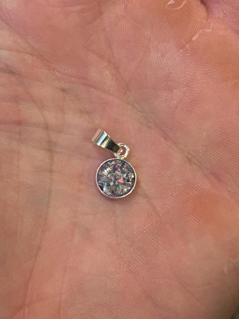 May include: A silver pendant with a round, clear glass charm filled with iridescent glitter.