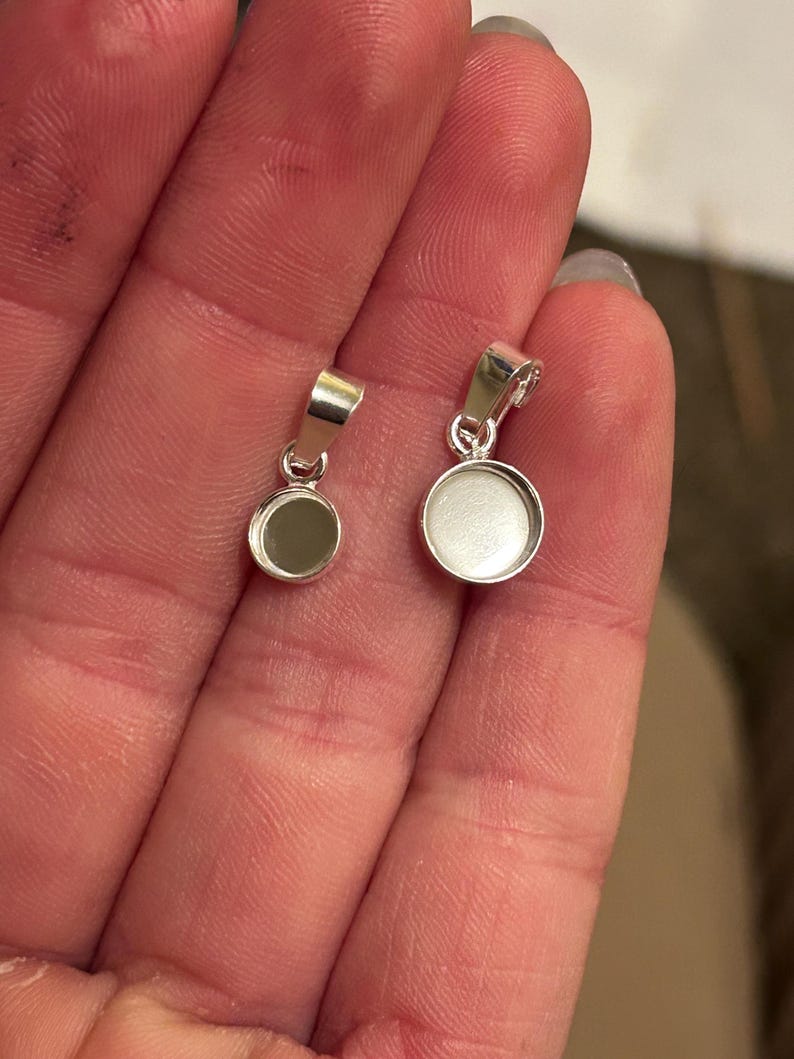 May include: Two silver pendant blanks with round bezels. The larger bezel is approximately 1 inch in diameter and the smaller bezel is approximately 3/4 inch in diameter.