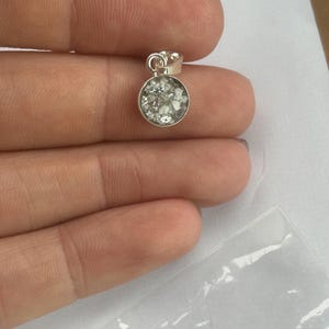 May include: A silver pendant with a round, clear glass insert filled with small white particles.