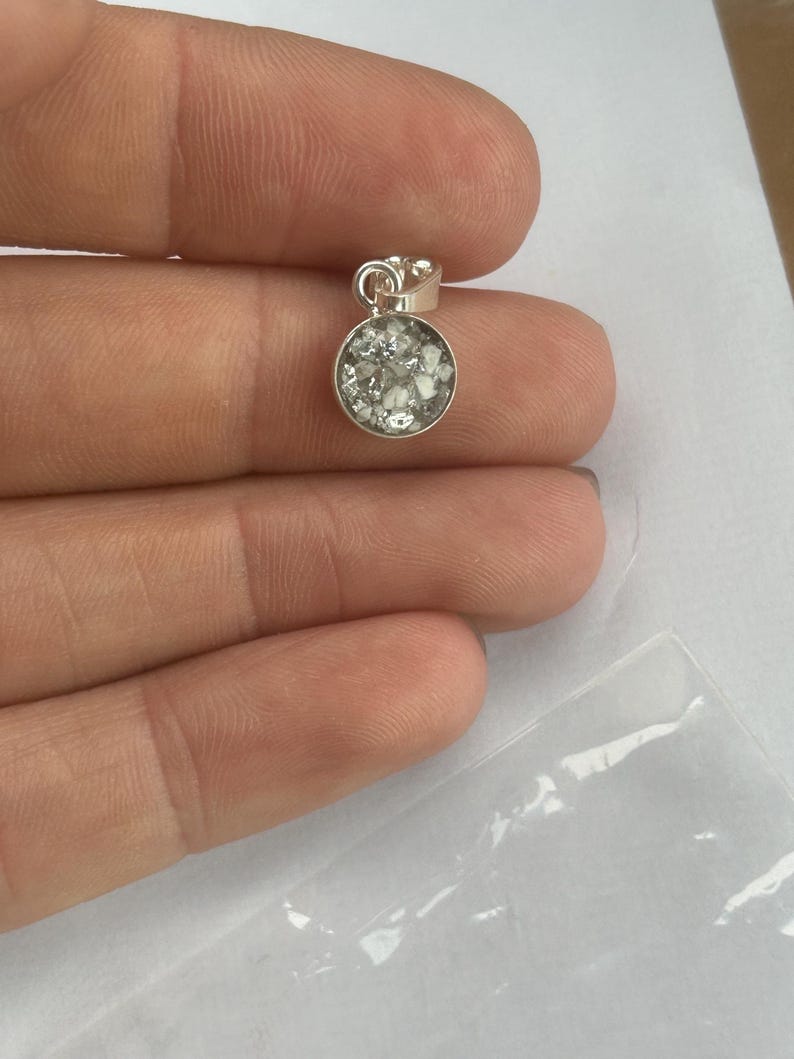 May include: A silver pendant with a round, clear glass insert filled with small white particles.