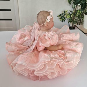 May include: A baby doll wearing a pink dress with a floral headband and butterfly wings. The dress has multiple layers of ruffled fabric and gold accents. The text "fedchyshyna_babydress" is visible.