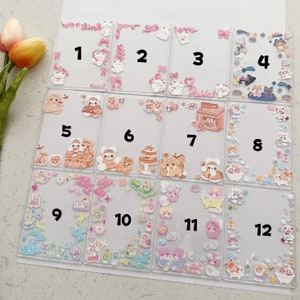 May include: Twelve clear plastic frames with numbers 1 through 12, each containing a variety of colorful, whimsical stickers and illustrations. The frames are arranged in a grid pattern.