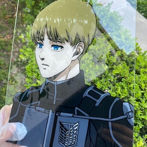 May include: A hand-painted glass panel featuring a character from the anime series, Attack on Titan. The artwork depicts a character with blonde hair and blue eyes, wearing a black uniform with a silver emblem. The background is blurred.