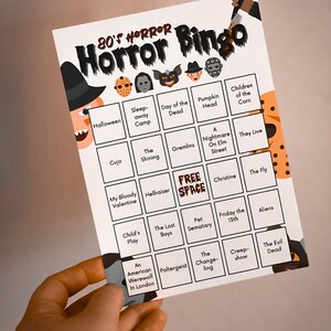 May include: A white 80's Horror Bingo card with a black border. The card features a witch, a knife, and various horror movie icons. The bingo card includes titles like "Halloween", "Gremlins", and "Friday the 13th".