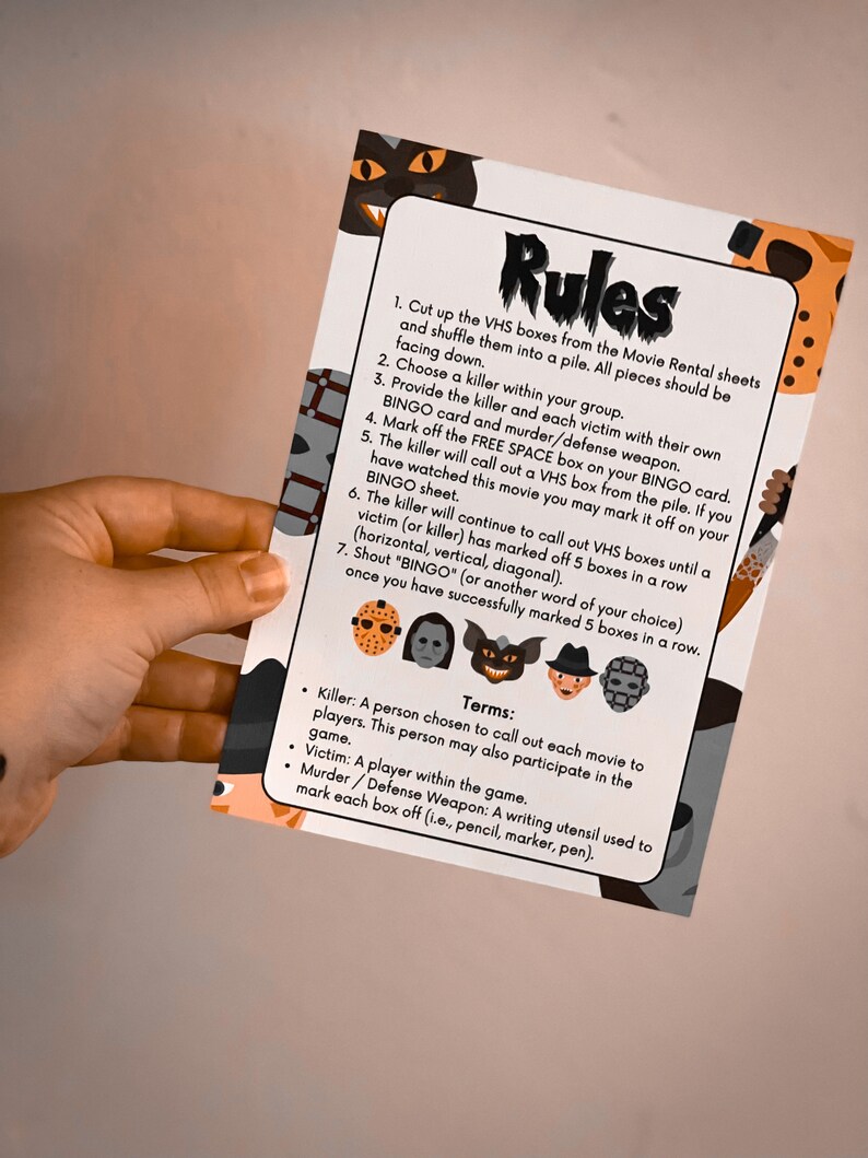 May include: A printed game card with the word "Rules" at the top. The card features instructions for a horror movie-themed bingo game, with illustrations of iconic movie villains. The card is held by a person.