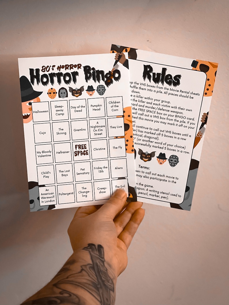 May include: A printed bingo game titled "80's Horror Bingo" with a Halloween theme. The game features a bingo card with movie titles like "Halloween" and "The Shining." The rules are printed on a separate sheet.