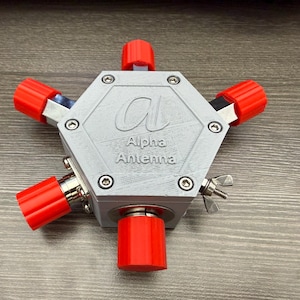 May include: A gray, hexagonal Alpha Antenna device with six red knobs. The device has a silver finish and is secured with screws. The Alpha Antenna logo is visible on the front.