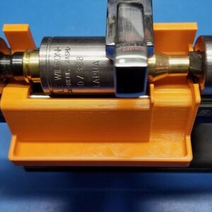 May include: Close-up of a metallic tool with the text "WILSON - LAPUA" printed on it, held in an orange 3D-printed holder. The tool is on a black base against a blue background.