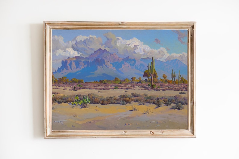 Puede incluir: Una pintura al &oacute;leo enmarcada que representa un paisaje des&eacute;rtico con monta&ntilde;as en el fondo. El cielo es de un azul claro con nubes blancas y esponjosas. En primer plano, hay una variedad de plantas del desierto, incluyendo cactus y arbustos. La pintura est&aacute; en un marco de madera claro.