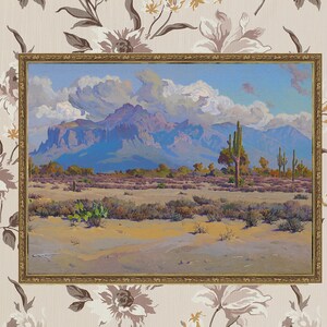 Puede incluir: Una pintura al &oacute;leo enmarcada que representa un paisaje des&eacute;rtico con monta&ntilde;as en el fondo. En primer plano se pueden ver varias plantas del desierto, incluyendo cactus y arbustos. El cielo es de un azul brillante con nubes blancas y esponjosas.