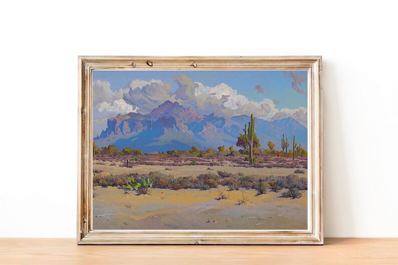 Puede incluir: Una pintura enmarcada que representa un paisaje des&eacute;rtico con una cordillera en el fondo. El cielo es azul con nubes blancas y el primer plano es un desierto arenoso con cactus y otras plantas del desierto.