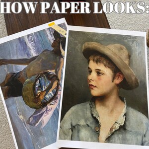 May include: Two framed paintings on a wooden surface. The painting on the left shows a man holding a basket of fish. The painting on the right shows a portrait of a young boy wearing a hat.