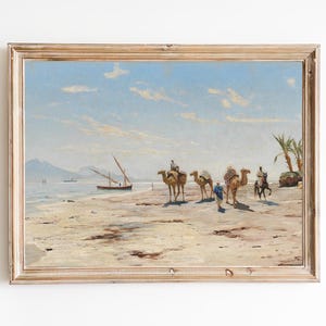 May include: A framed oil painting depicting a beach scene with camels and riders. The painting features a light blue sky with white clouds, a sandy beach, and a calm sea. In the distance, a small boat sails on the water. The camels are walking along the beach, and the riders are wearing traditional clothing.