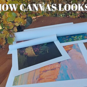 May include: Three rolled up canvases with different paintings. The top canvas shows a blue and green floral design. The middle canvas shows a still life of a basket of red cherries. The bottom canvas shows a landscape with orange and blue hues.