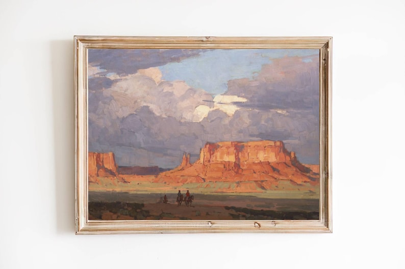 May include: A framed painting depicting a desert landscape with red rock formations and a cloudy sky. The painting features a group of figures on horseback in the foreground.