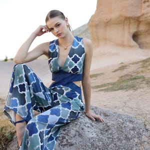 May include: A two-piece outfit featuring a sleeveless top and wide-leg pants. The top has a deep V-neck and a cutout design, while the pants have a high waist. Both pieces are patterned with a blue and white geometric design.