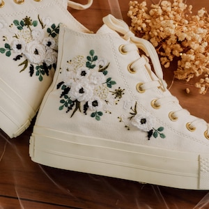 Könnte beinhalten: Weiße High-Top-Canvas-Sneaker mit gestickten weißen Blumen und grünen Blättern.