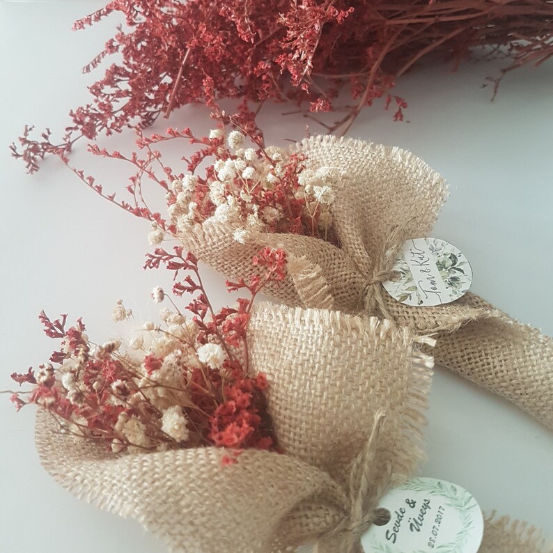 May include: Two small bouquets of dried flowers wrapped in burlap fabric. The bouquets are tied with twine and have a small round tag attached with the text "Tara & Kyle" and "Savie & Always 5.27.2017".