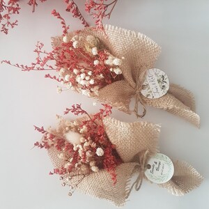 May include: Two small bouquets of dried flowers wrapped in burlap with a circular tag attached to each. The tag on the left bouquet says "Tom & Kat" and the tag on the right bouquet says "Sande & Nanya 21.07.2017".