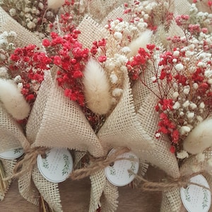 May include: Small bouquets of dried flowers wrapped in burlap fabric with a twine bow and a round tag with text. The flowers are white and red.