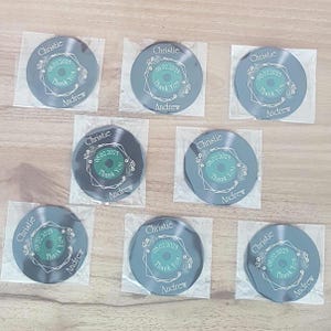 May include: Eight black vinyl record-shaped thank you favors with a green and white floral design. The text on the favors reads "Christie & Andrew 08.02.2025 Thank You".