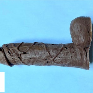 May include: A brown rubber toy with a textured surface. The toy has a bulbous head and a long, cylindrical body.