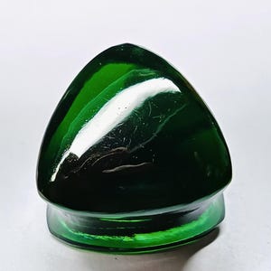 May include: A dark green glass bottle stopper with a triangular top and a rounded base. The stopper has a glossy finish and reflects light, creating highlights. The product is likely for wine or other bottled beverages.