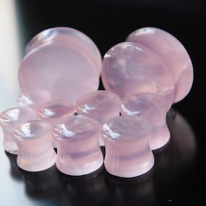 May include: A set of pink stone ear gauges in various sizes. The gauges are made of a translucent pink stone with a smooth, polished finish.
