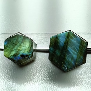 May include: Two hexagonal labradorite gemstone rings. The gemstones display a mix of green and blue iridescent colors. The rings are set on a silver band. The gemstones are approximately 1 inch in diameter.