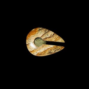 May include: A teardrop-shaped stone ear gauge with a brown, tan, and white marbled pattern. The gauge has a hole in the center.